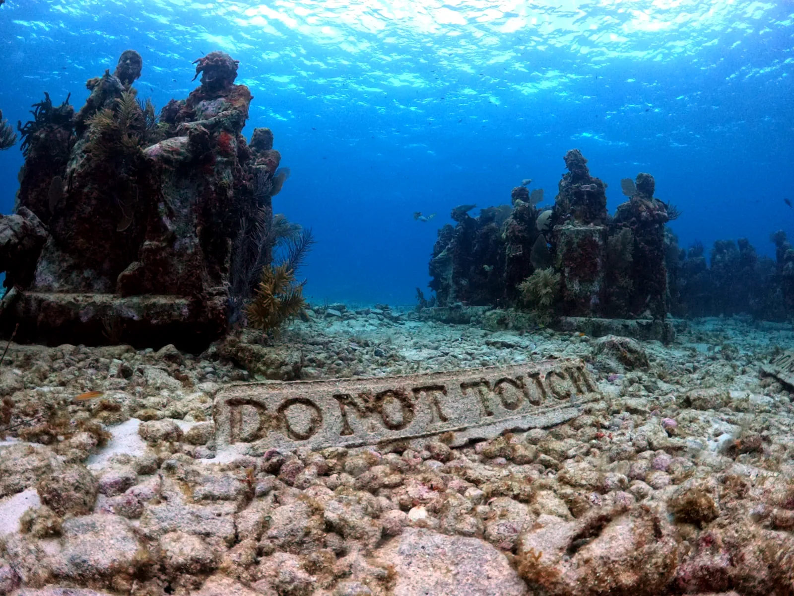 MUSA sculptures behind a carved 'Do not touch' sign on the sand