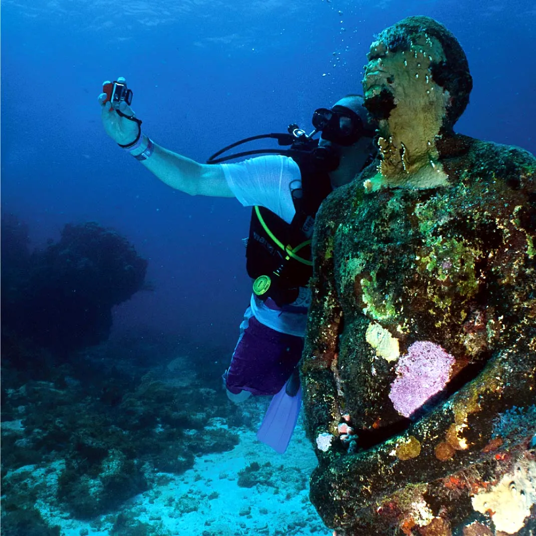 Buzo fotografiando una escultura del MUSA cubierta de coral